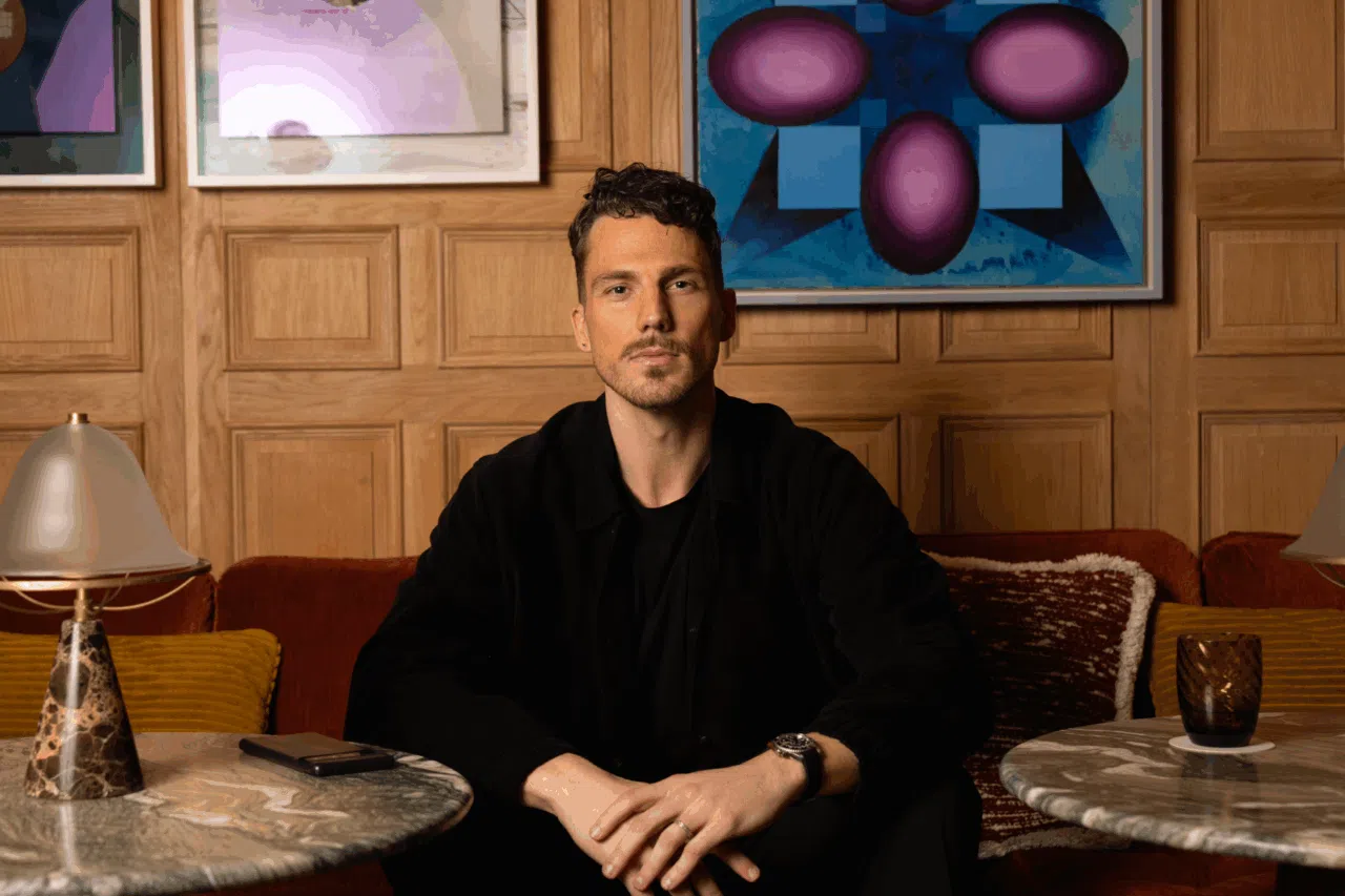 Portrait of Olle Olsson, CSO of ASPACE, seated in a warmly lit lounge with wood-paneled walls and abstract artwork in the background. He is dressed in black, looking confidently at the camera.