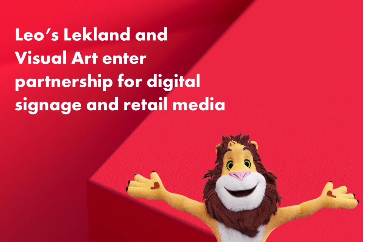 Red promotional graphic with white text reading “Leo’s Lekland and Visual Art enter partnership for digital signage and retail media.” At the bottom right, a cheerful cartoon lion mascot with outstretched arms smiles toward the viewer against a bold red geometric background.